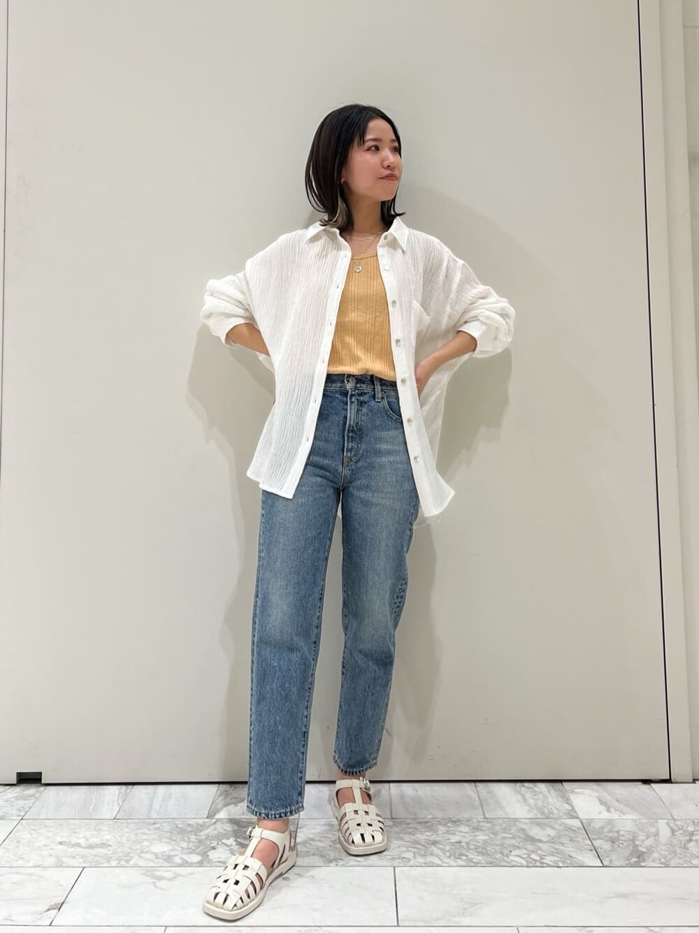 ブルー系のデニムパンツ、オレンジ系のタンクトップ、ホワイト系のシャツ/ブラウスを着用したレディースの春コーディネートの2枚目の写真