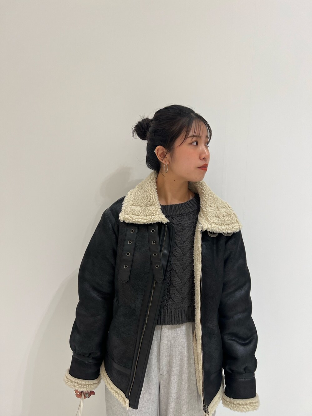 ホワイト系のハンドバッグ、グレー系のニット/セーター、ブラック系のムートンコートを着用したレディースの冬コーディネートの2枚目の写真