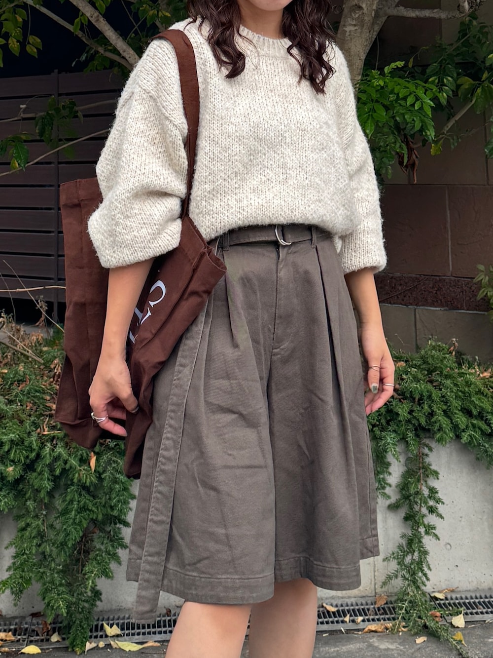 グレー系のチノパンツ、ホワイト系のニット/セーター、ブラウン系のトートバッグを着用したレディースの秋コーディネートの3枚目の写真