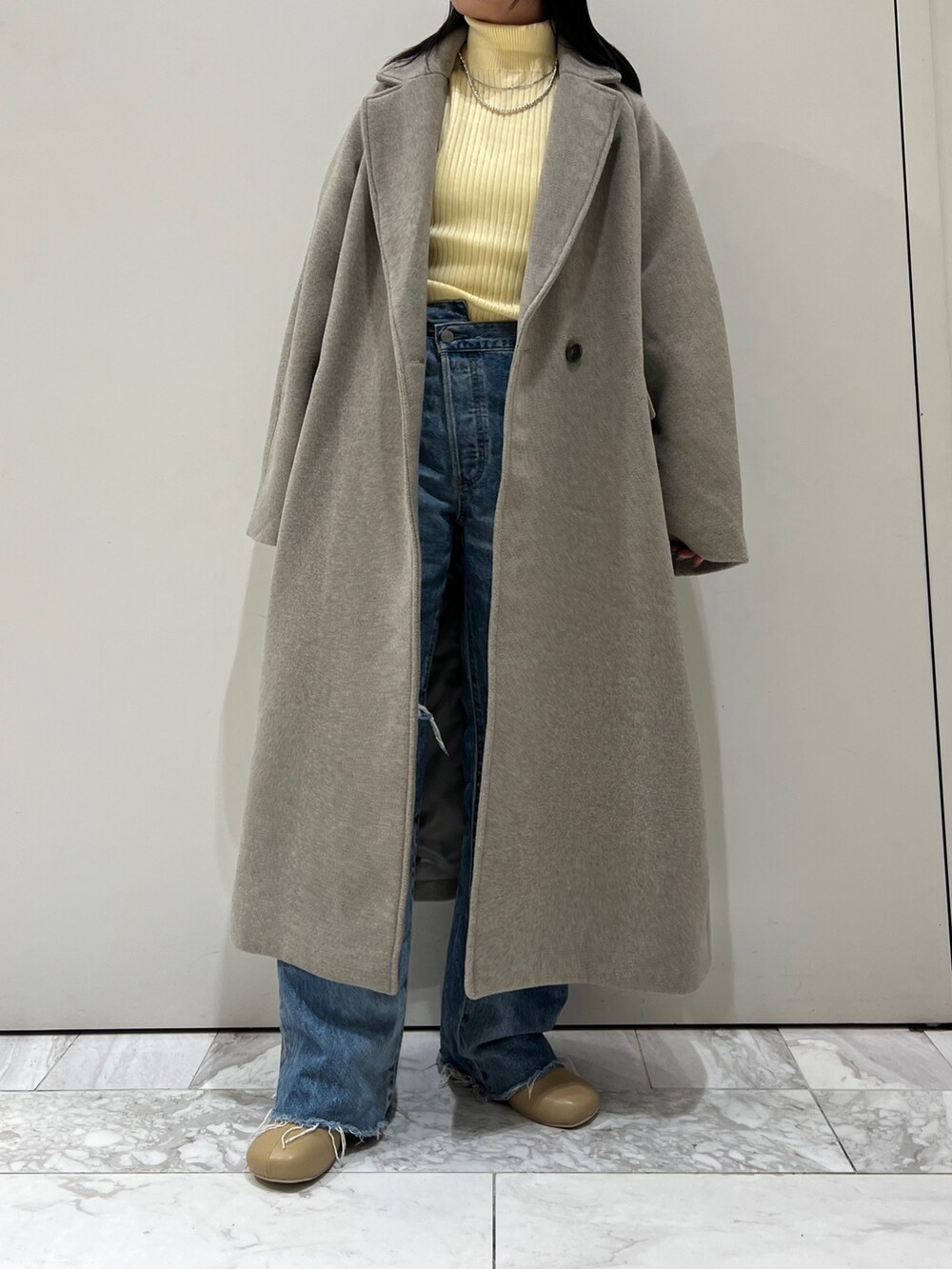 グレー系のチェスターコート、イエロー系のニット/セーター、ブルー系のデニムパンツを着用したレディースの秋コーディネートの2枚目の写真