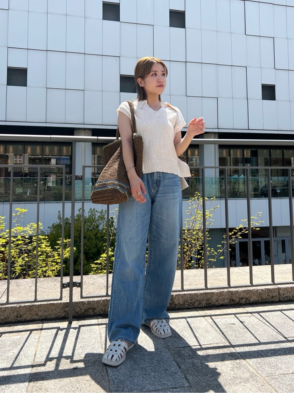 ブラウン系のトートバッグ、ブルー系のデニムパンツ、ホワイト系のサンダルを着用したレディースの春コーディネートの3枚目の写真