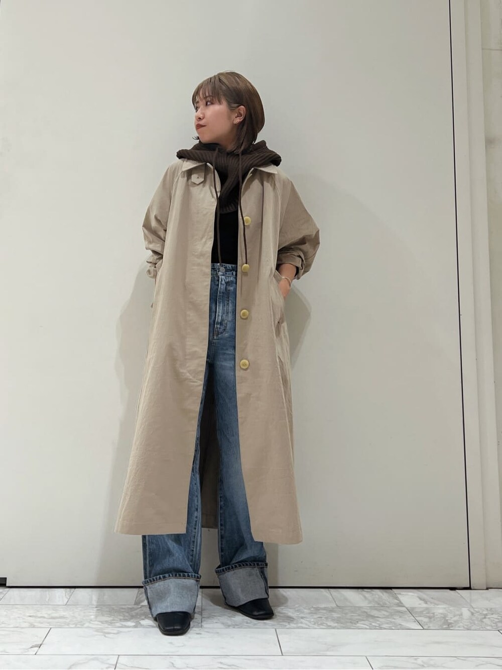 ベージュ系のステンカラーコート、ブラック系のブーツ、ブルー系のデニムパンツを着用したレディースの秋コーディネートの2枚目の写真