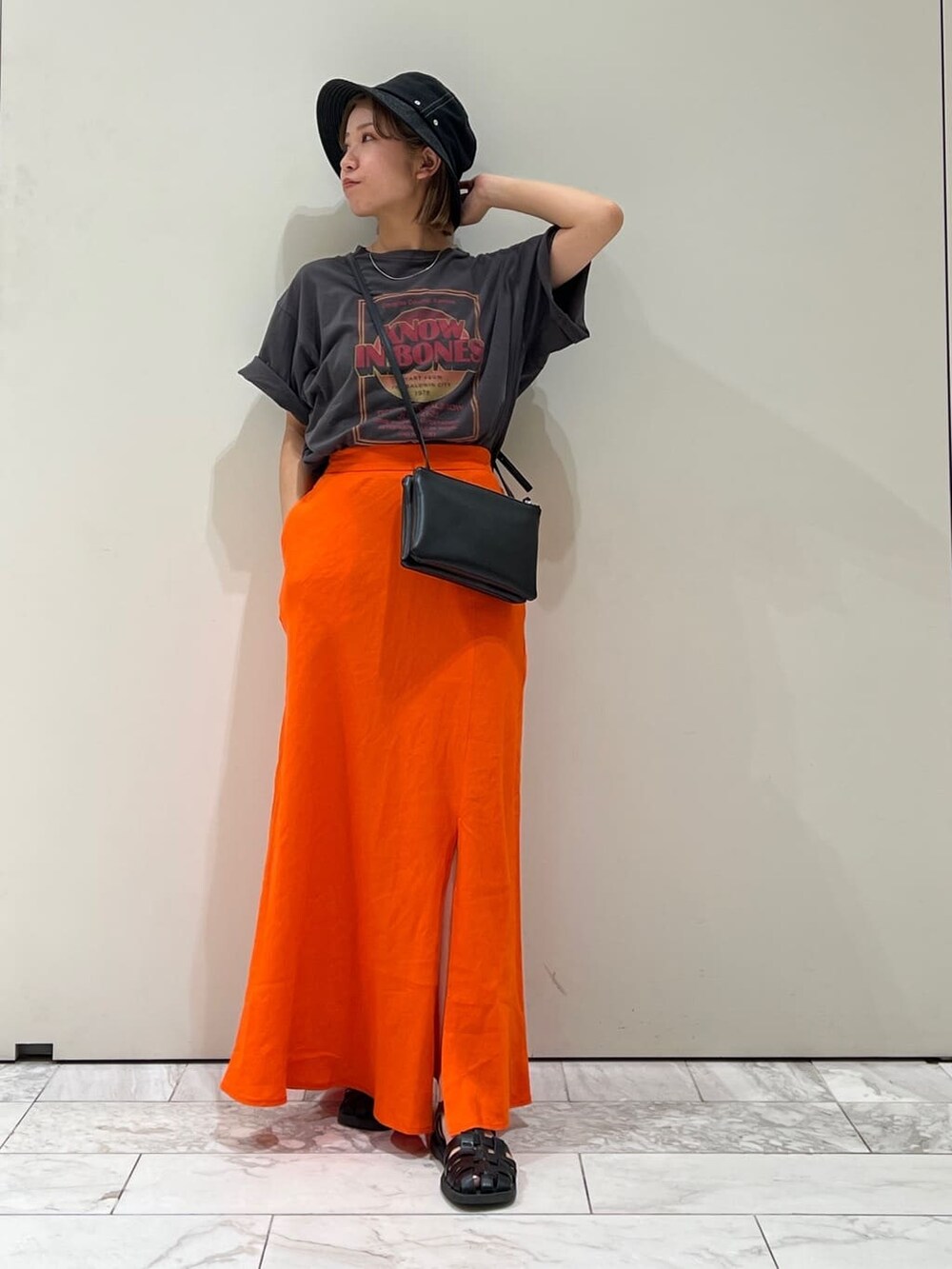ブラック系のショルダーバッグ、グレー系のTシャツ/カットソー、オレンジ系のスカートを着用したレディースの夏コーディネートの7枚目の写真