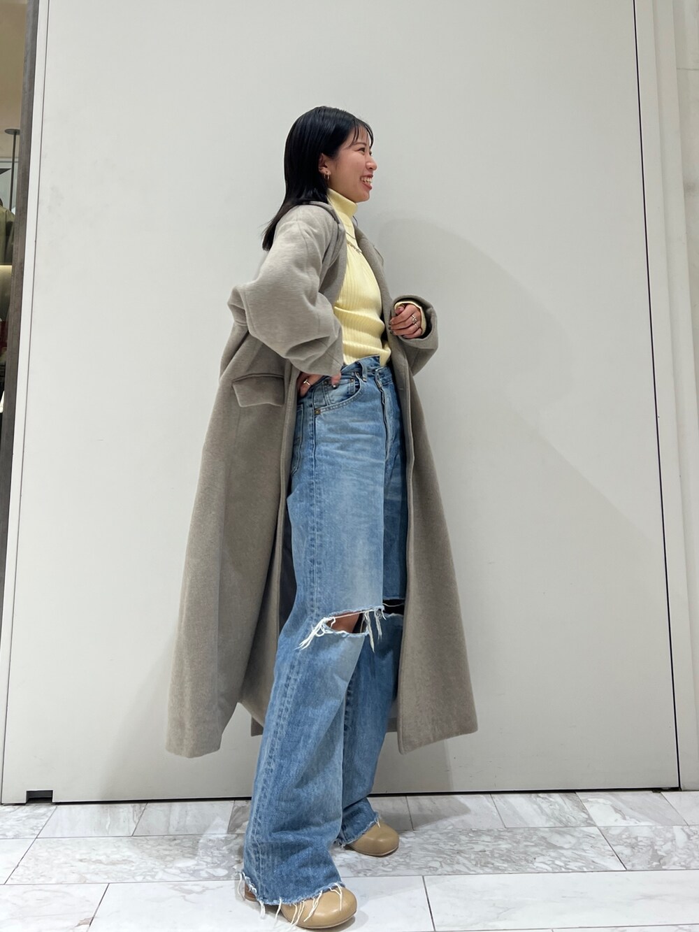 グレー系のチェスターコート、イエロー系のニット/セーター、ブルー系のデニムパンツを着用したレディースの秋コーディネートの3枚目の写真