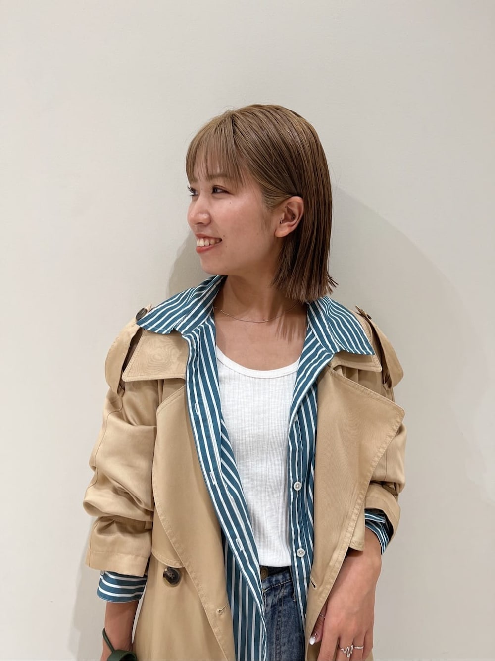 ベージュ系のトレンチコート、グリーン系のシャツ/ブラウス、ブルー系のデニムパンツを着用したレディースの夏コーディネートの6枚目の写真