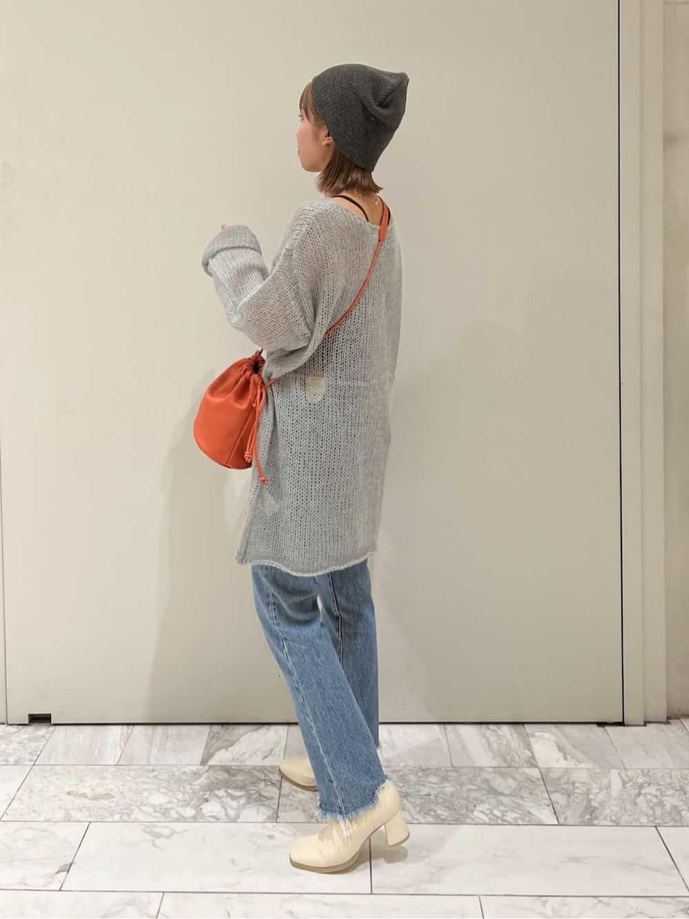 オレンジ系のハンドバッグ、ホワイト系のブーツ、ブルー系のデニムパンツを着用したレディースの秋コーディネートの3枚目の写真