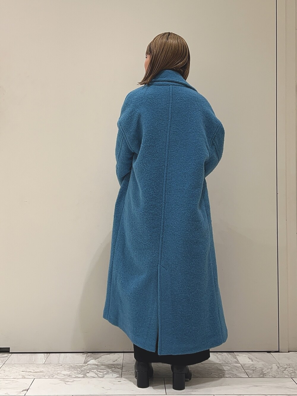 ブルー系のチェスターコート、ブラック系のワンピース、ブラック系のブーツを着用したレディースの冬コーディネートの3枚目の写真