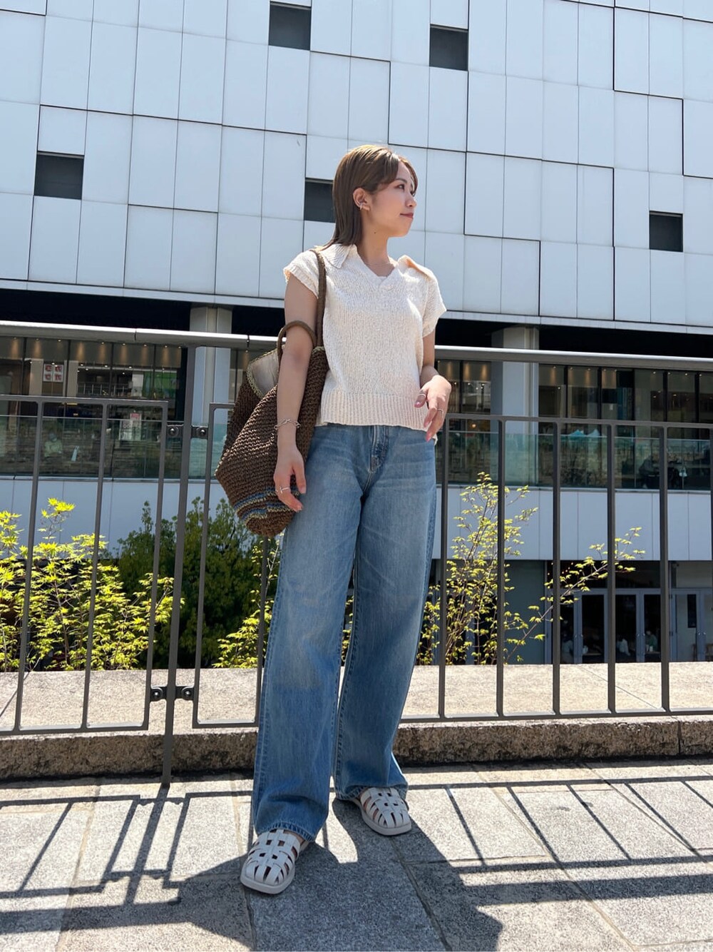 ブラウン系のトートバッグ、ブルー系のデニムパンツ、ホワイト系のサンダルを着用したレディースの春コーディネートの4枚目の写真