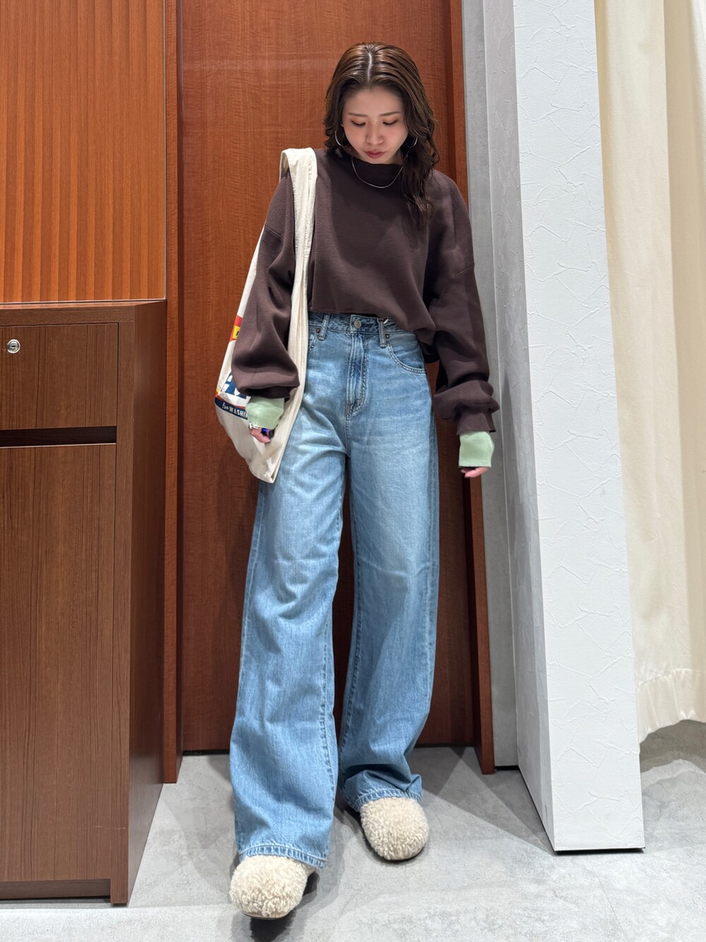 ブルー系のデニムパンツ、ブラウン系のニット/セーター、ホワイト系のトートバッグを着用したレディースの冬コーディネートの2枚目の写真