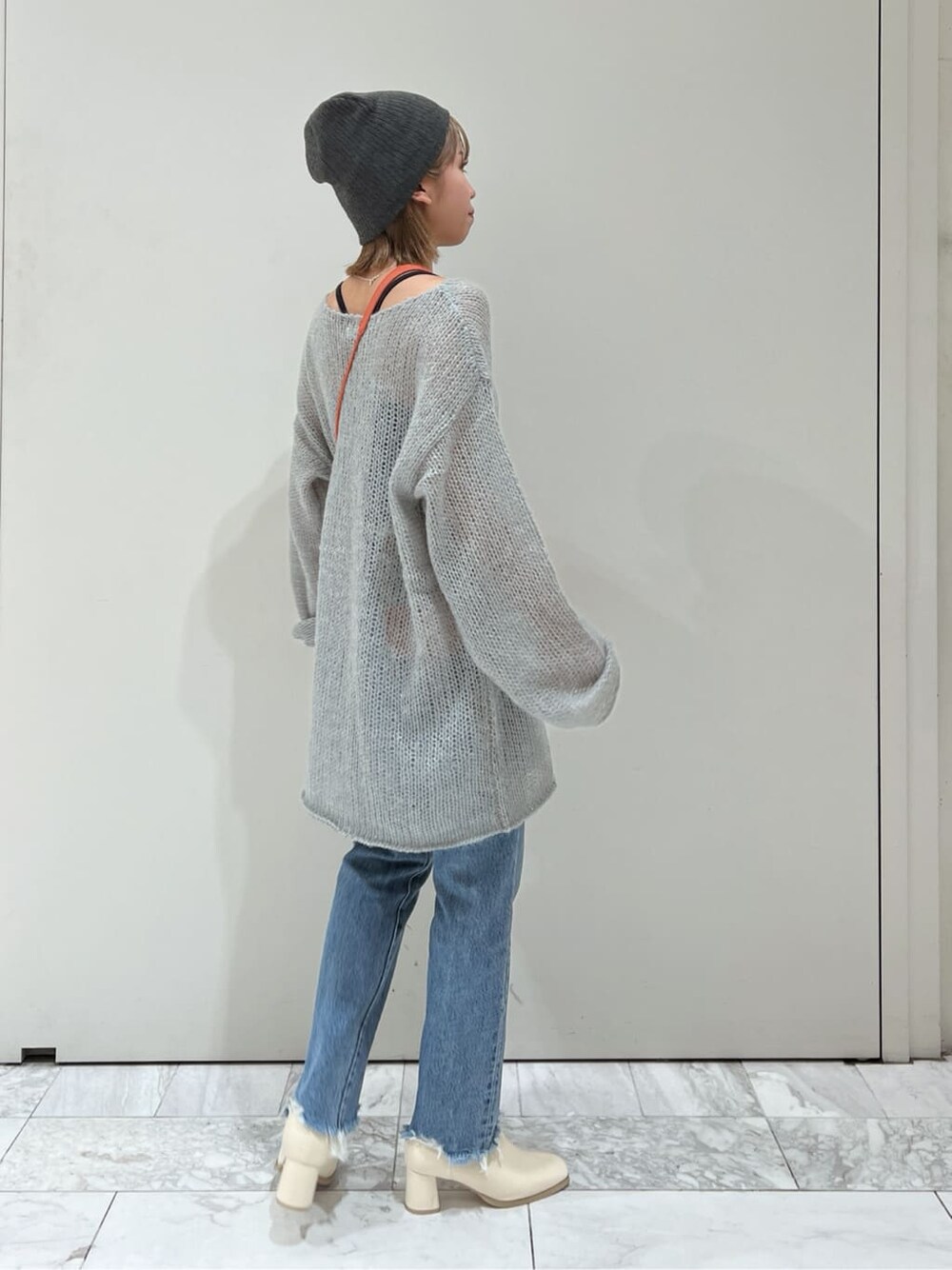 オレンジ系のハンドバッグ、ホワイト系のブーツ、ブルー系のデニムパンツを着用したレディースの秋コーディネートの5枚目の写真