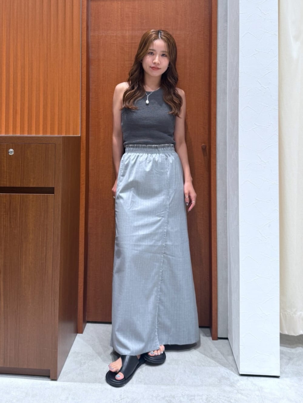 グレー系のニット/セーター、グレー系のスカート、シルバー系のネックレスを着用したレディースの夏コーディネートの5枚目の写真