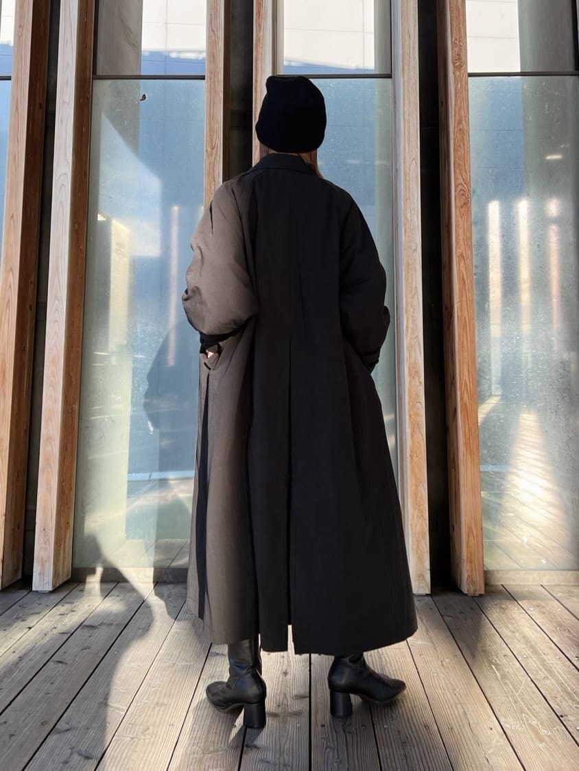 ブラック系のステンカラーコート、グリーン系のワンピース、ブラック系のブーツを着用したレディースの秋コーディネートの6枚目の写真