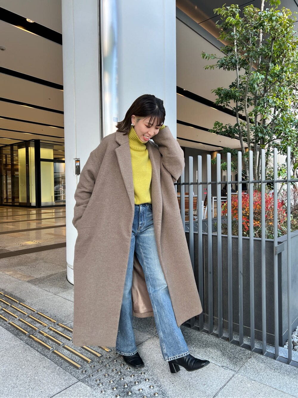 ベージュ系のチェスターコート、ブルー系のデニムパンツ、グリーン系のニット/セーターを着用したレディースの冬コーディネートの2枚目の写真