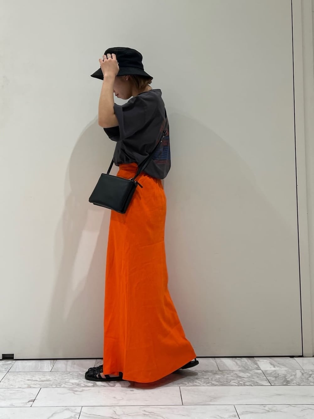 ブラック系のショルダーバッグ、グレー系のTシャツ/カットソー、オレンジ系のスカートを着用したレディースの夏コーディネートの2枚目の写真