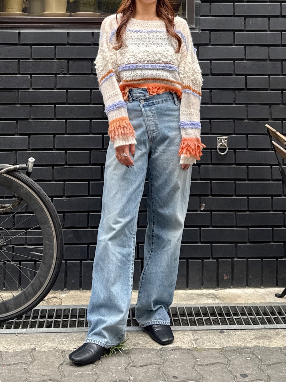 ブルー系のデニムパンツ、ホワイト系のニット/セーター、ブラック系のサンダルを着用したレディースの秋コーディネートの2枚目の写真