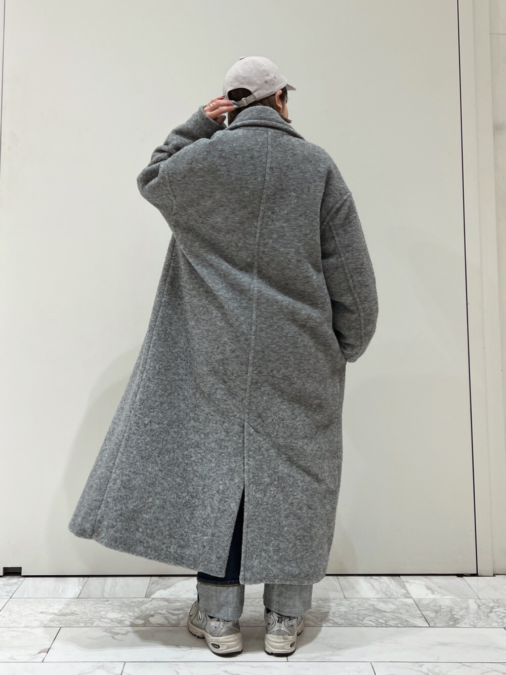 グレー系のチェスターコート、グリーン系のニット/セーター、グレー系のキャップを着用したレディースの冬コーディネートの6枚目の写真