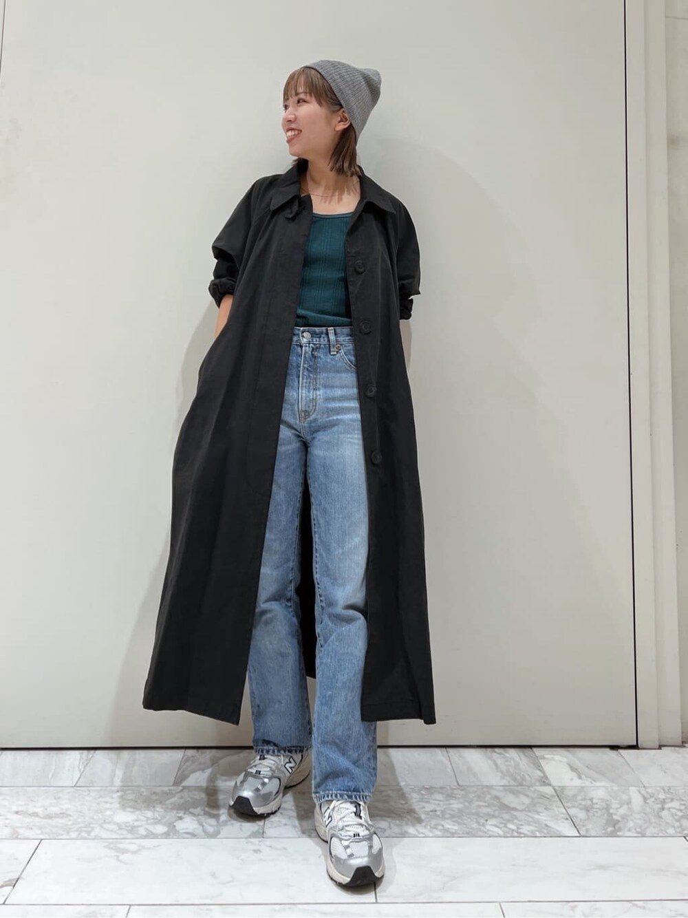 ブラック系のステンカラーコート、グリーン系のTシャツ/カットソー、ブルー系のデニムパンツを着用したレディースの秋コーディネートの3枚目の写真