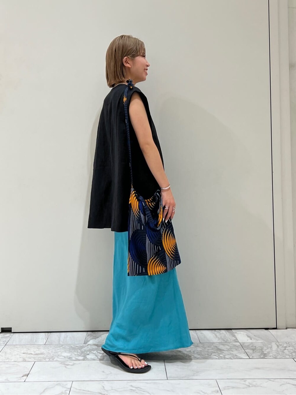 ブラック系のベスト、ブラック系のサンダル、ブルー系のスカートを着用したレディースの夏コーディネートの2枚目の写真