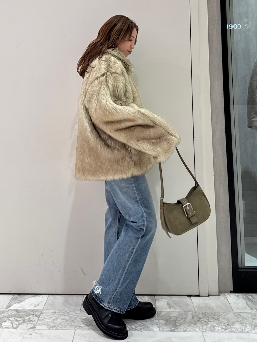 ベージュ系のダウンジャケット/コート、グリーン系のハンドバッグ、ブルー系のデニムパンツを着用したレディースの冬コーディネートの2枚目の写真