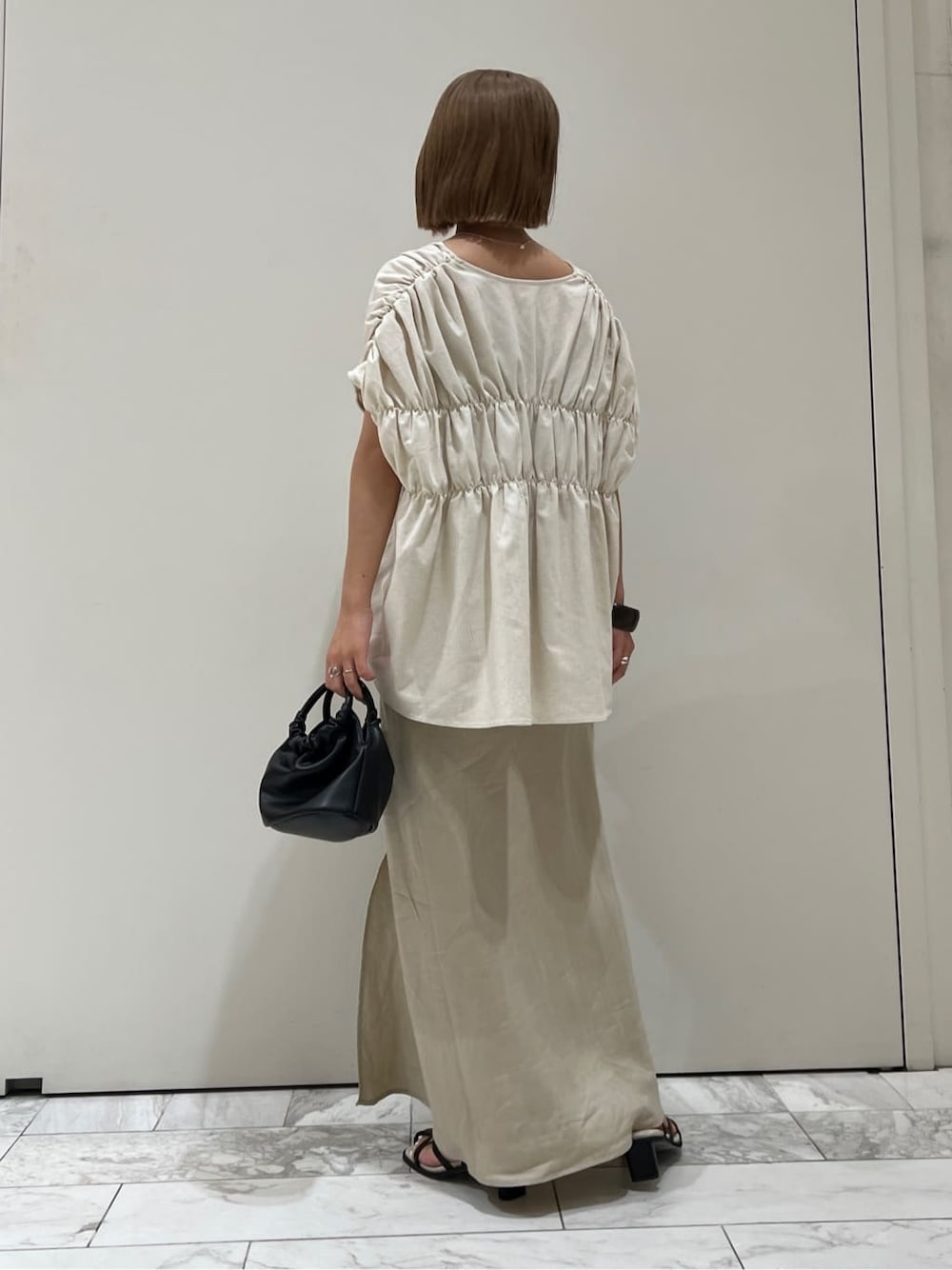 ブラック系のサンダル、ベージュ系のスカート、ホワイト系のシャツ/ブラウスを着用したレディースの夏コーディネートの5枚目の写真