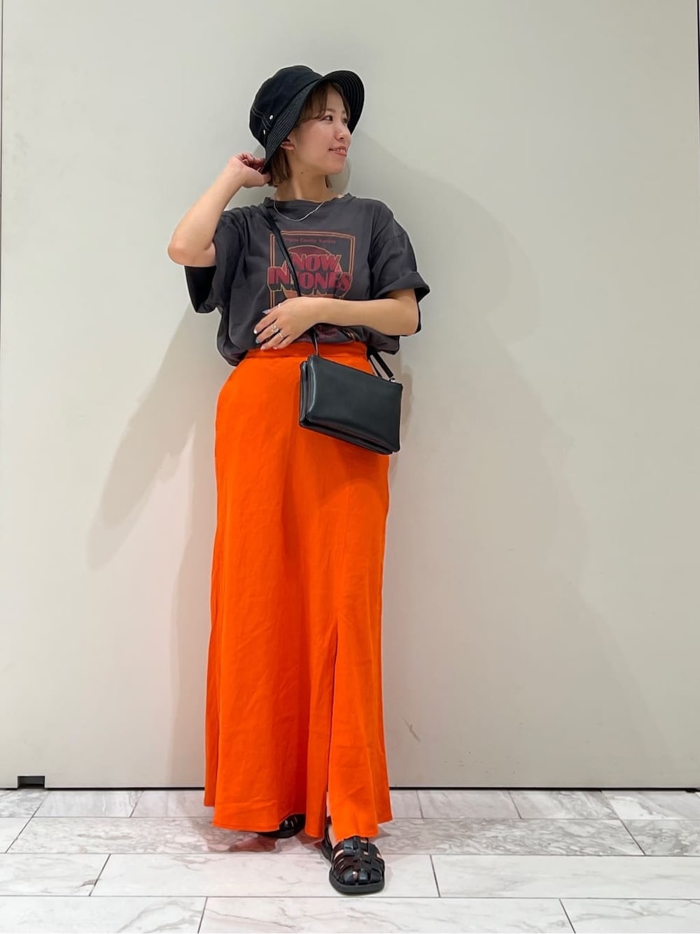 ブラック系のショルダーバッグ、グレー系のTシャツ/カットソー、オレンジ系のスカートを着用したレディースの夏コーディネートの6枚目の写真