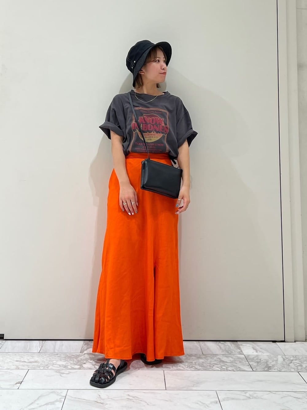 ブラック系のショルダーバッグ、グレー系のTシャツ/カットソー、オレンジ系のスカートを着用したレディースの夏コーディネートの5枚目の写真
