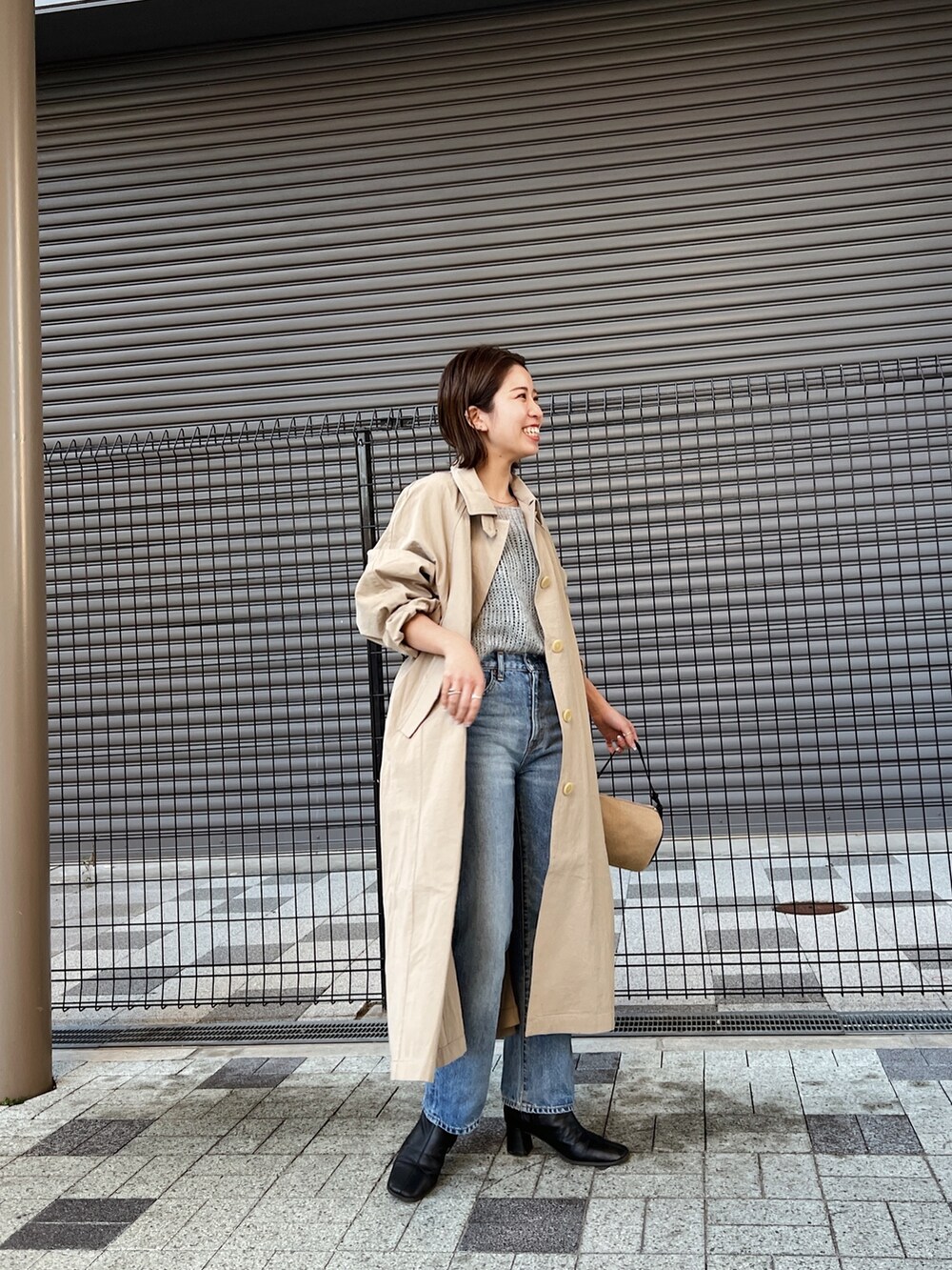 ブルー系のデニムパンツ、ベージュ系のステンカラーコート、グレー系のニット/セーターを着用したレディースの冬コーディネートの2枚目の写真