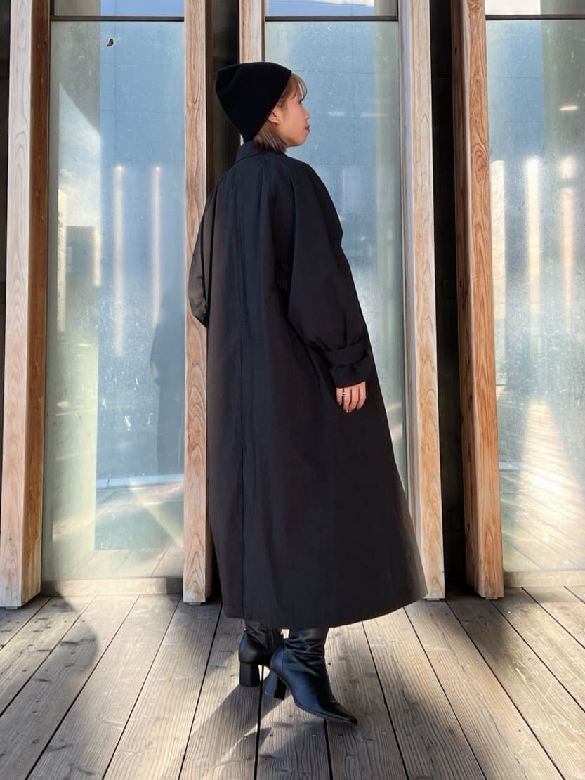 ブラック系のステンカラーコート、グリーン系のワンピース、ブラック系のブーツを着用したレディースの秋コーディネートの5枚目の写真