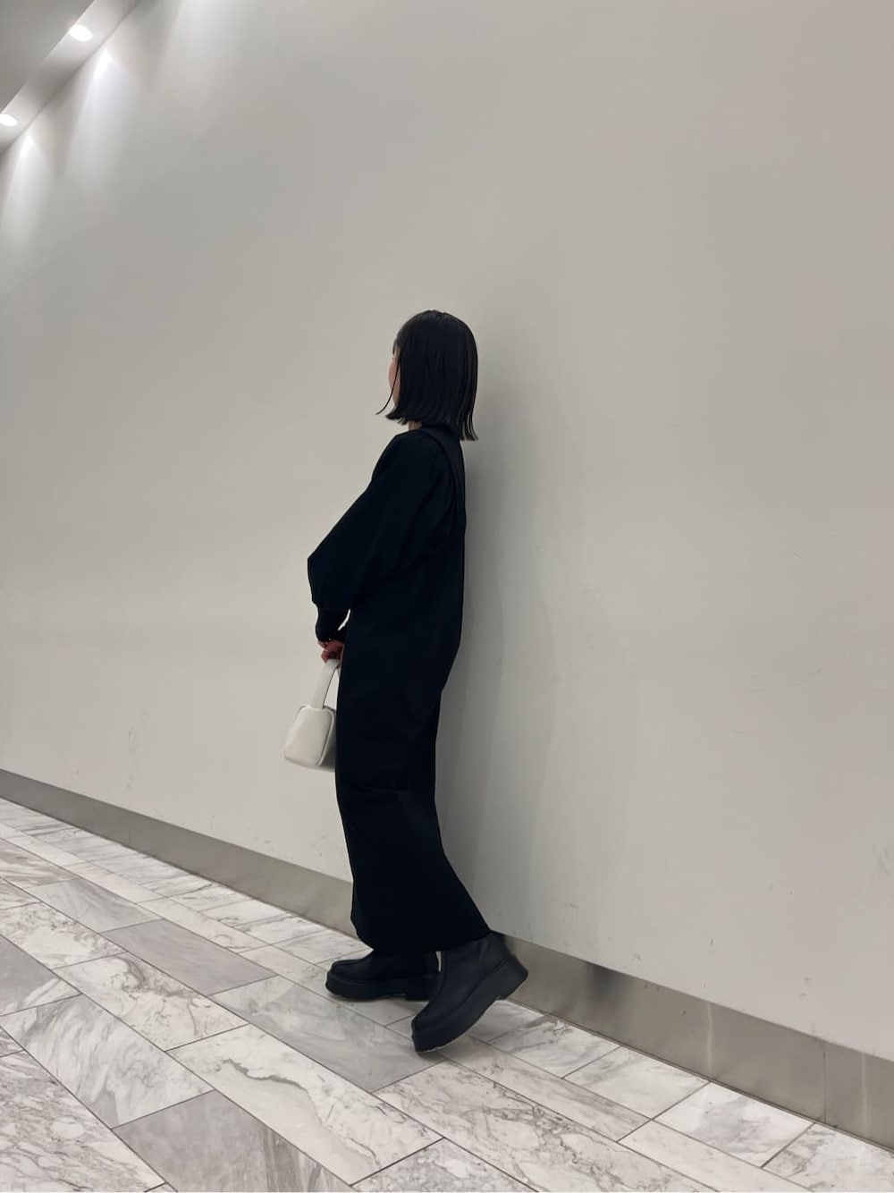 ブラック系のワンピース、ブラック系のブーツ、ホワイト系のハンドバッグを着用したレディースの冬コーディネートの4枚目の写真