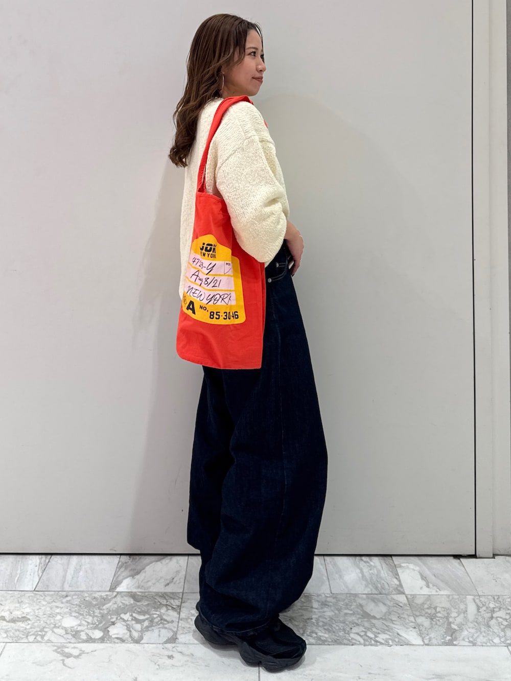 ブルー系のデニムパンツ、ホワイト系のニット/セーター、オレンジ系のトートバッグを着用したレディースの冬コーディネートの3枚目の写真