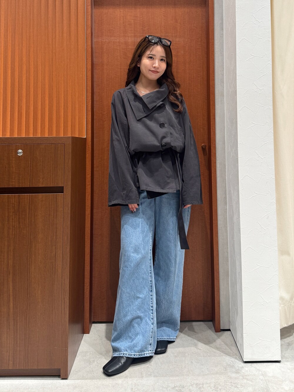 グレー系のトレンチコート、ブルー系のデニムパンツ、シルバー系のネックレスを着用したレディースの秋コーディネートの2枚目の写真