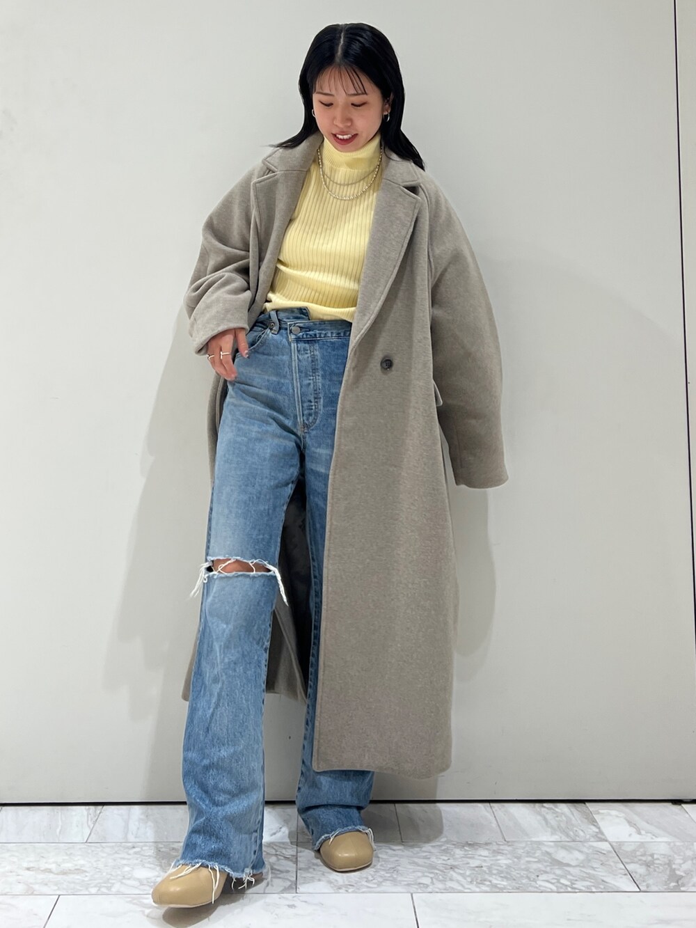 グレー系のチェスターコート、イエロー系のニット/セーター、ブルー系のデニムパンツを着用したレディースの秋コーディネートの10枚目の写真
