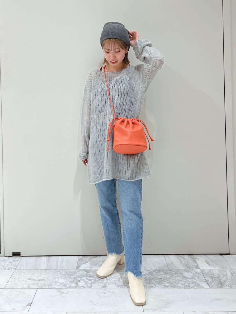 オレンジ系のハンドバッグ、ホワイト系のブーツ、ブルー系のデニムパンツを着用したレディースの秋コーディネートの2枚目の写真