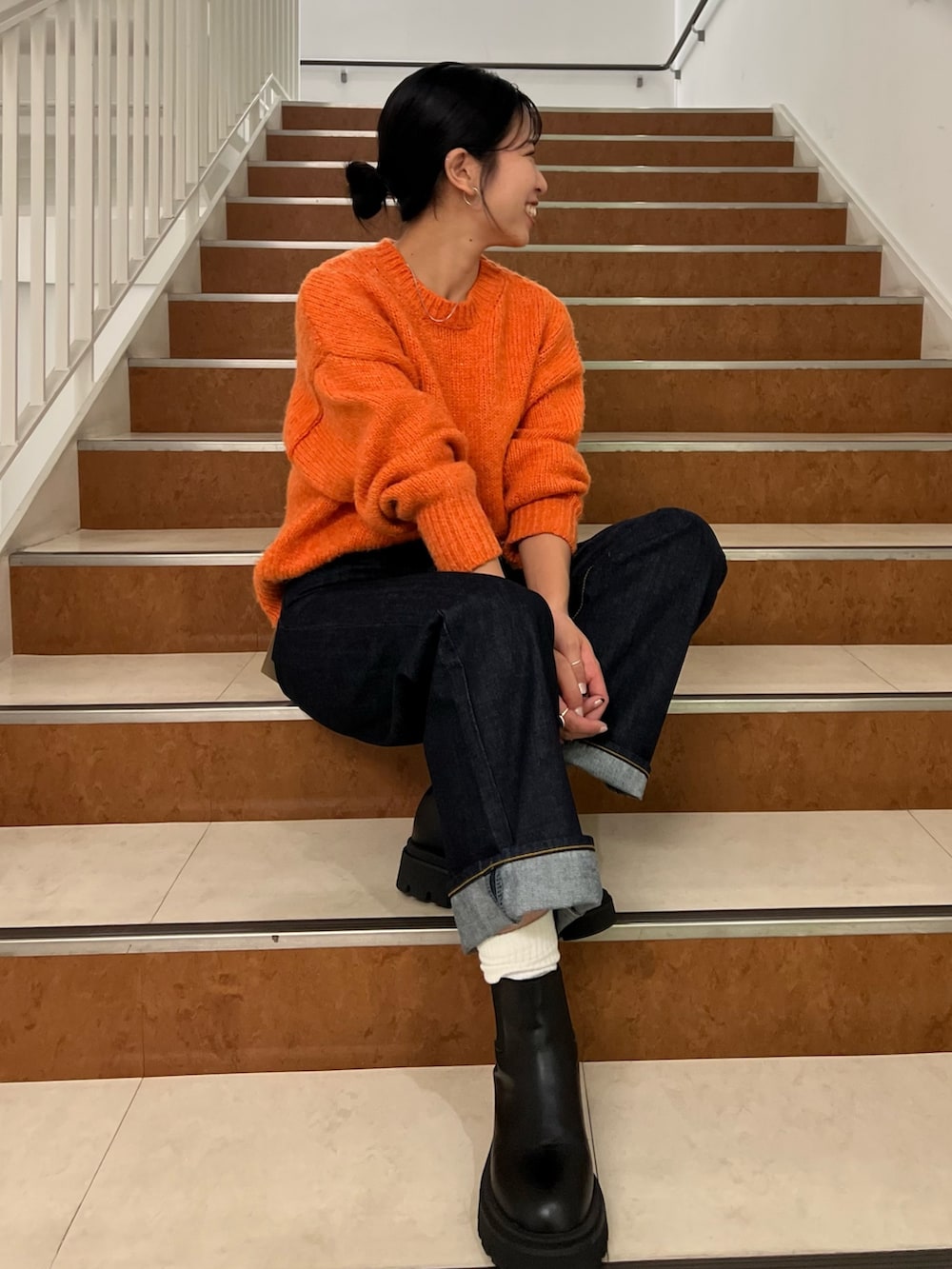 オレンジ系のニット/セーター、ブルー系のデニムパンツ、ホワイト系のダウンジャケット/コートを着用したレディースの秋コーディネートの8枚目の写真