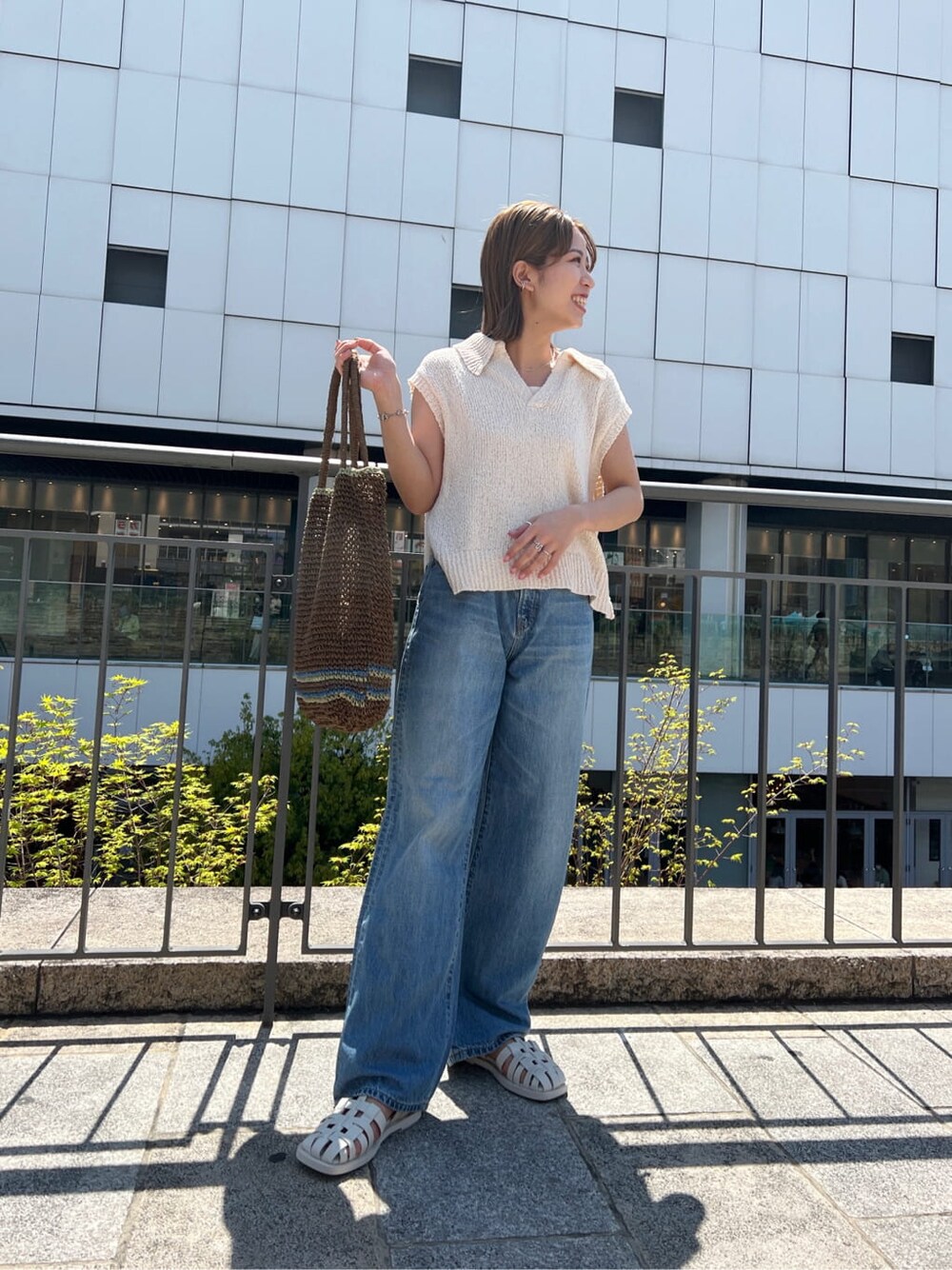 ブラウン系のトートバッグ、ブルー系のデニムパンツ、ホワイト系のサンダルを着用したレディースの春コーディネートの5枚目の写真