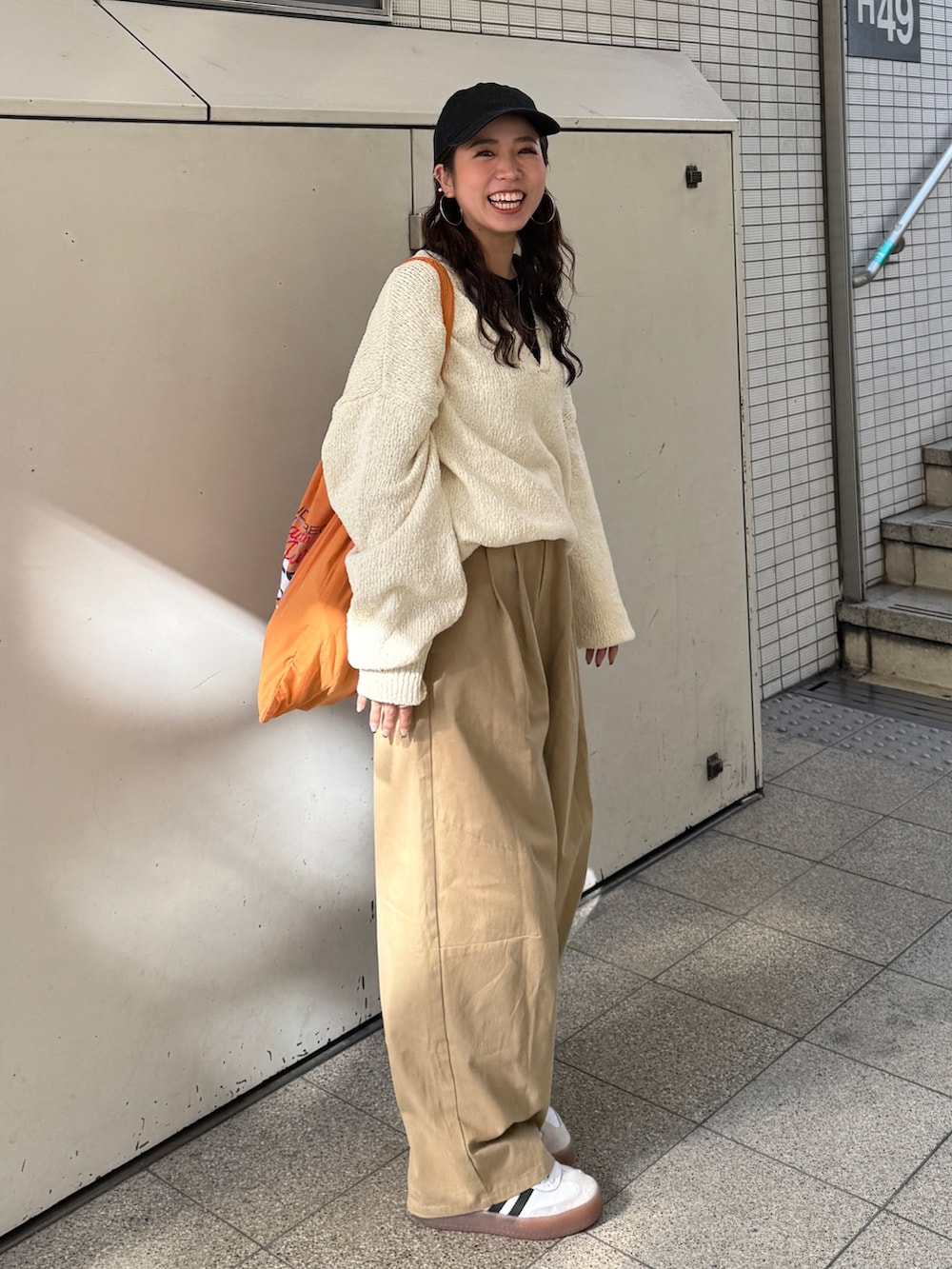 ベージュ系のチノパンツ、ホワイト系のニット/セーター、オレンジ系のエコバッグ/サブバッグを着用したレディースの冬コーディネートの2枚目の写真