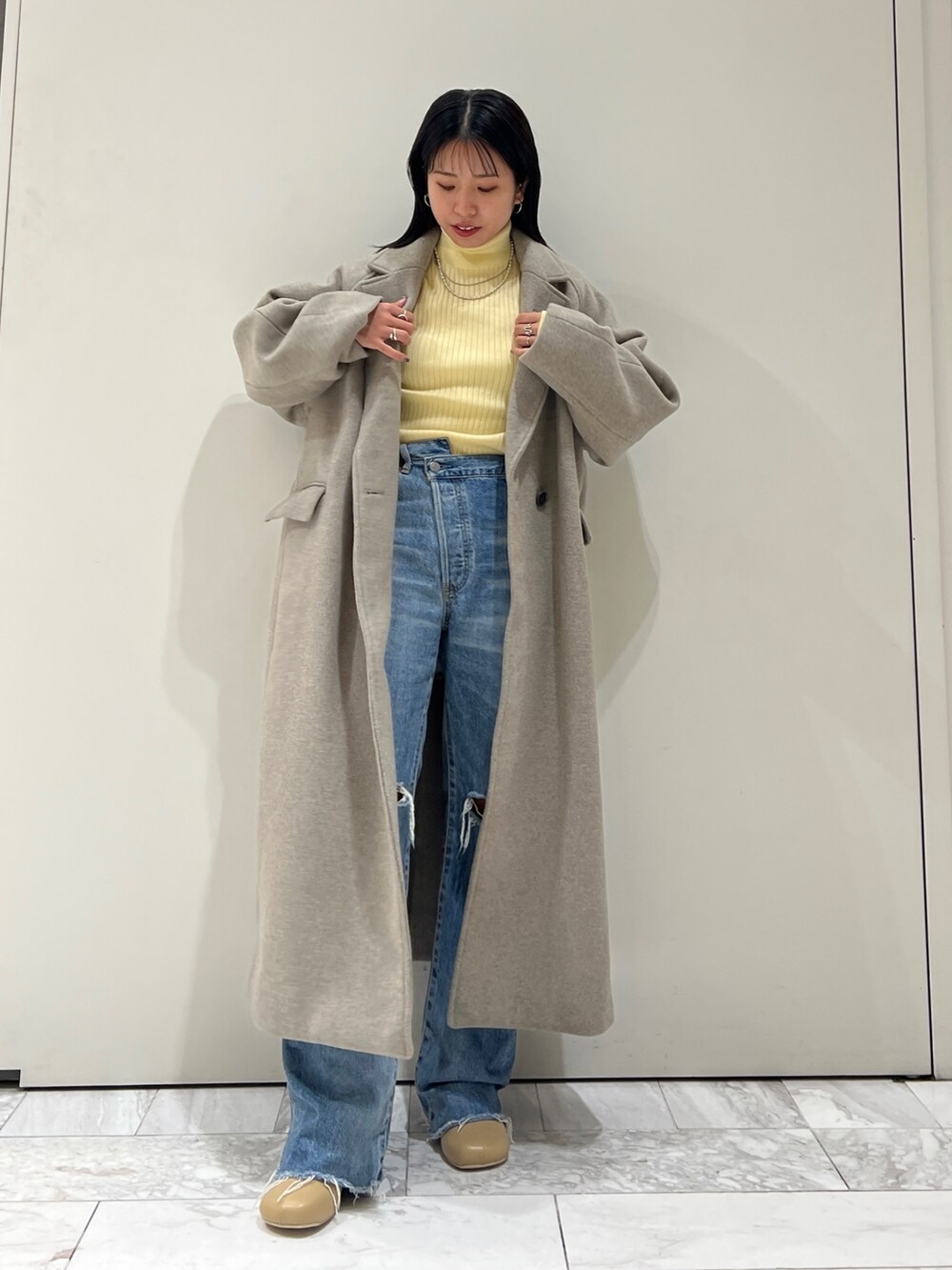 グレー系のチェスターコート、イエロー系のニット/セーター、ブルー系のデニムパンツを着用したレディースの秋コーディネートの6枚目の写真