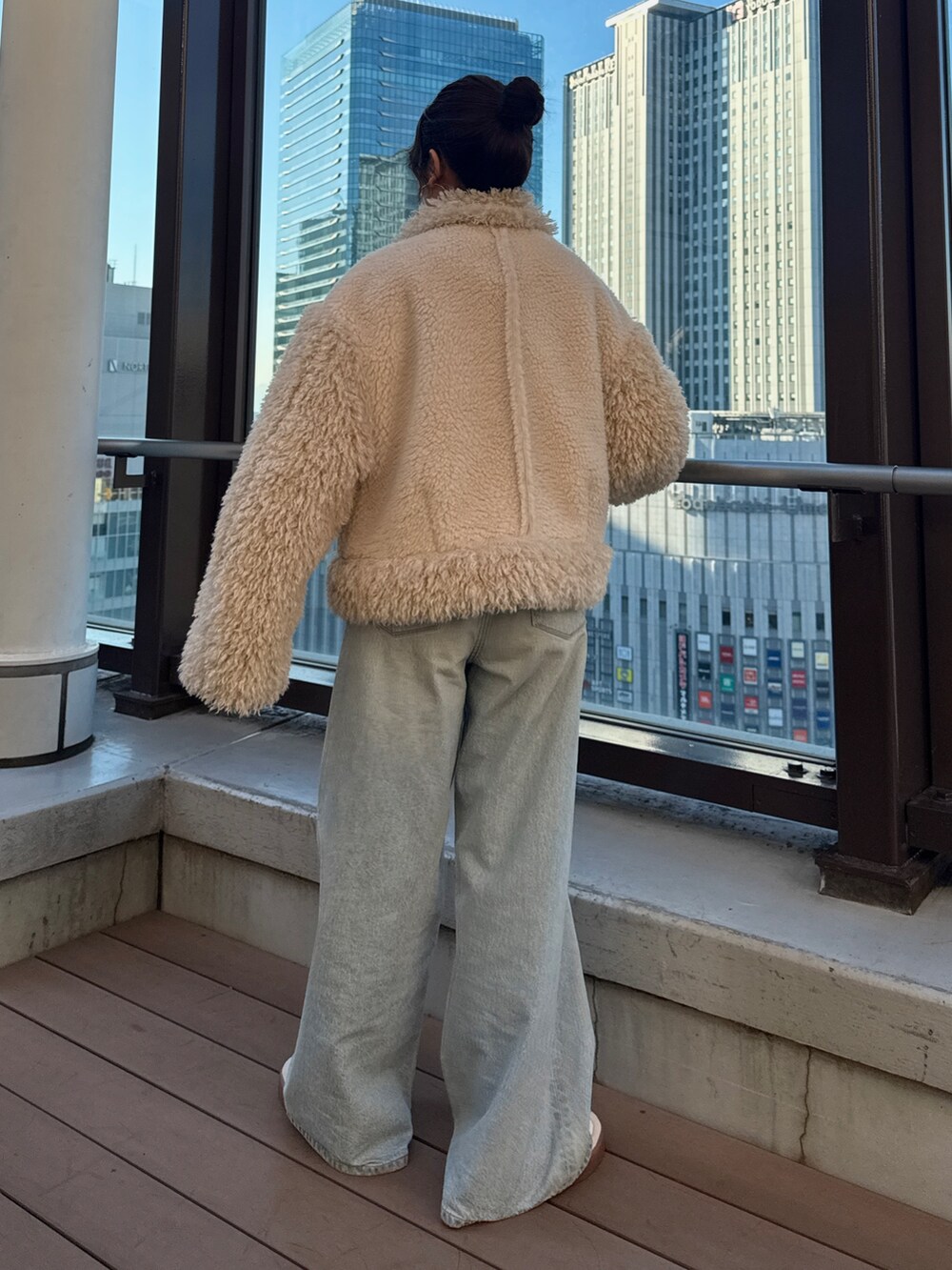 ホワイト系のムートンコート、グリーン系のニット/セーター、ブルー系のデニムパンツを着用したレディースの冬コーディネートの4枚目の写真