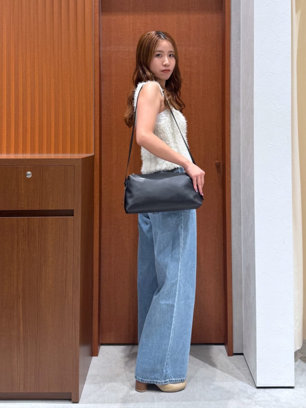 ブルー系のデニムパンツ、ホワイト系のベスト、ブラック系のハンドバッグを着用したレディースの夏コーディネートの2枚目の写真