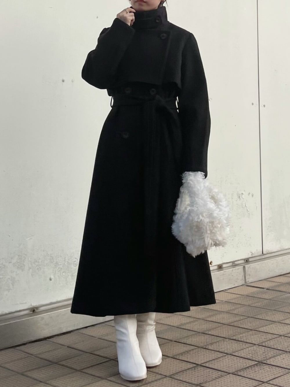 ホワイト系のハンドバッグ、ブラック系のトレンチコート、ホワイト系のブーツを着用したレディースの秋コーディネートの2枚目の写真