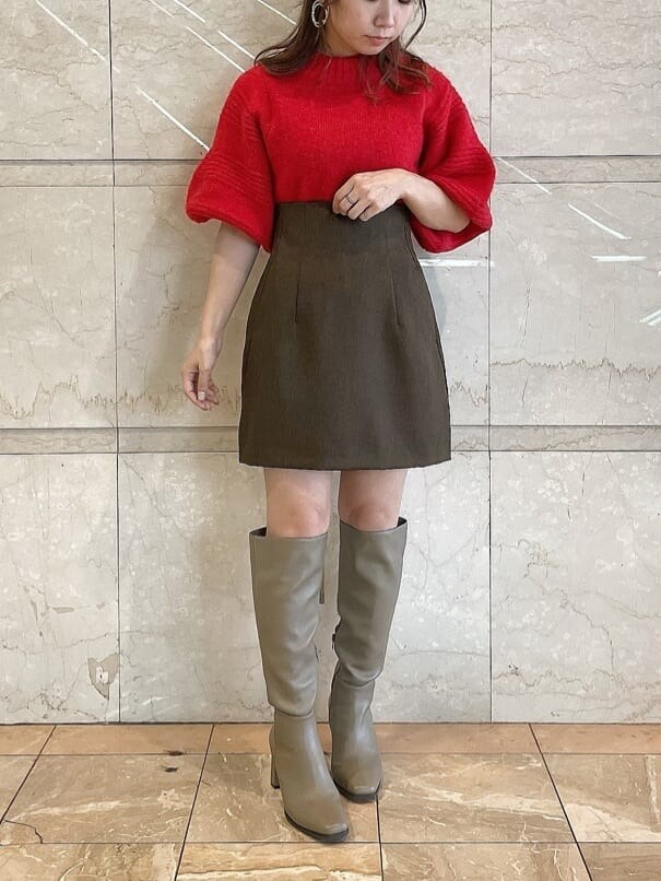 レッド系のニット/セーター、ブラウン系のスカート、ベージュ系のブーツを着用したレディースの秋コーディネートの2枚目の写真