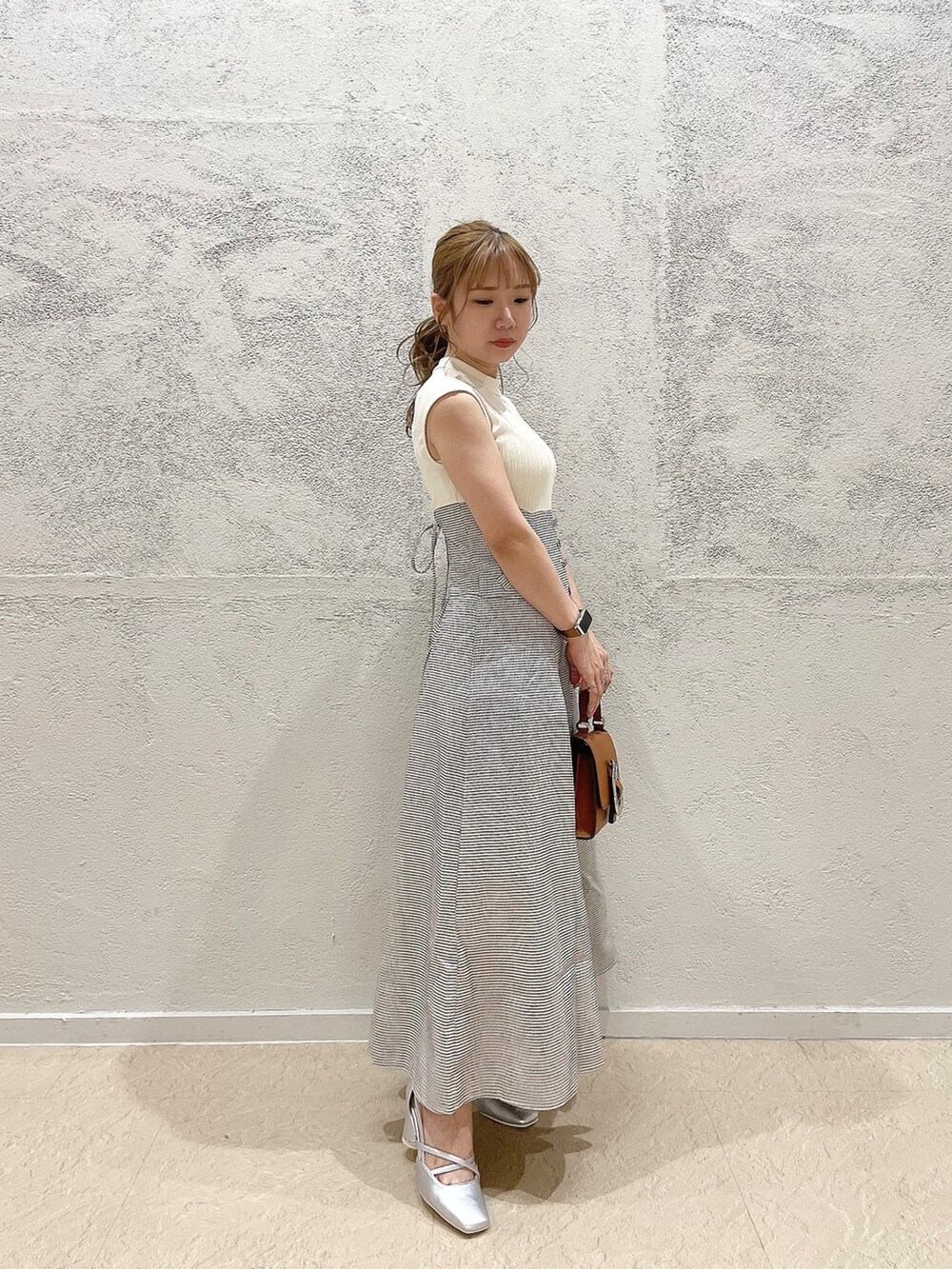 イエロー系のハンドバッグ、ホワイト系のワンピース、シルバー系のパンプスを着用したレディースの夏コーディネートの4枚目の写真