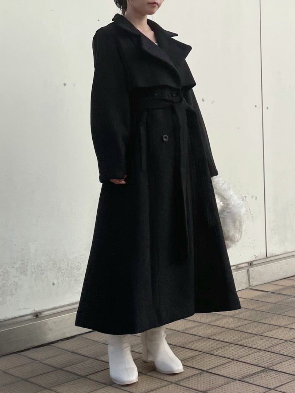 ホワイト系のハンドバッグ、ブラック系のトレンチコート、ホワイト系のブーツを着用したレディースの秋コーディネートの3枚目の写真