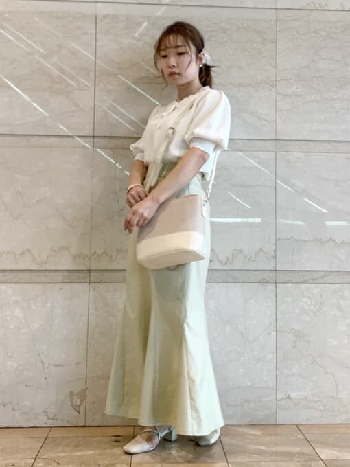 グリーン系のスカート、ホワイト系のパンプス、ホワイト系のハンドバッグを着用したレディースの春コーディネートの2枚目の写真