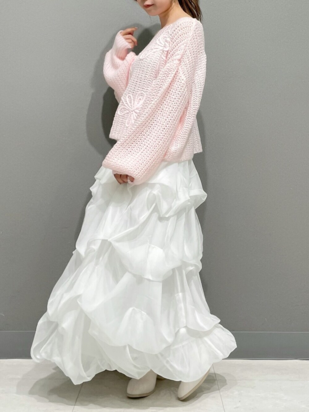 ピンク系のニット/セーター、ホワイト系のスカート、ホワイト系のブーツを着用したレディースの秋コーディネートの2枚目の写真