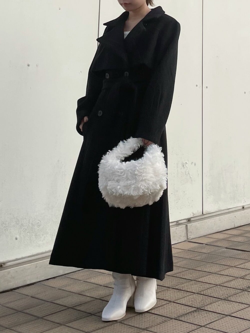 ホワイト系のハンドバッグ、ブラック系のトレンチコート、ホワイト系のブーツを着用したレディースの秋コーディネートの7枚目の写真