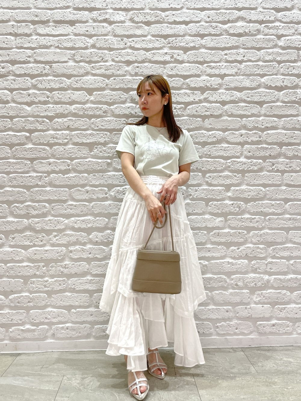 グリーン系のTシャツ/カットソー、ホワイト系のスカート、シルバー系のパンプスを着用したレディースの春コーディネートの2枚目の写真