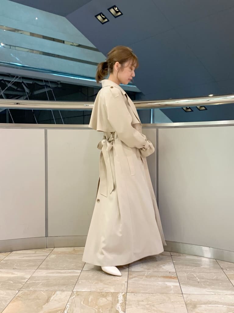 ベージュ系のトレンチコート、オレンジ系のワンピース、ホワイト系のパンプスを着用したレディースの冬コーディネートの8枚目の写真