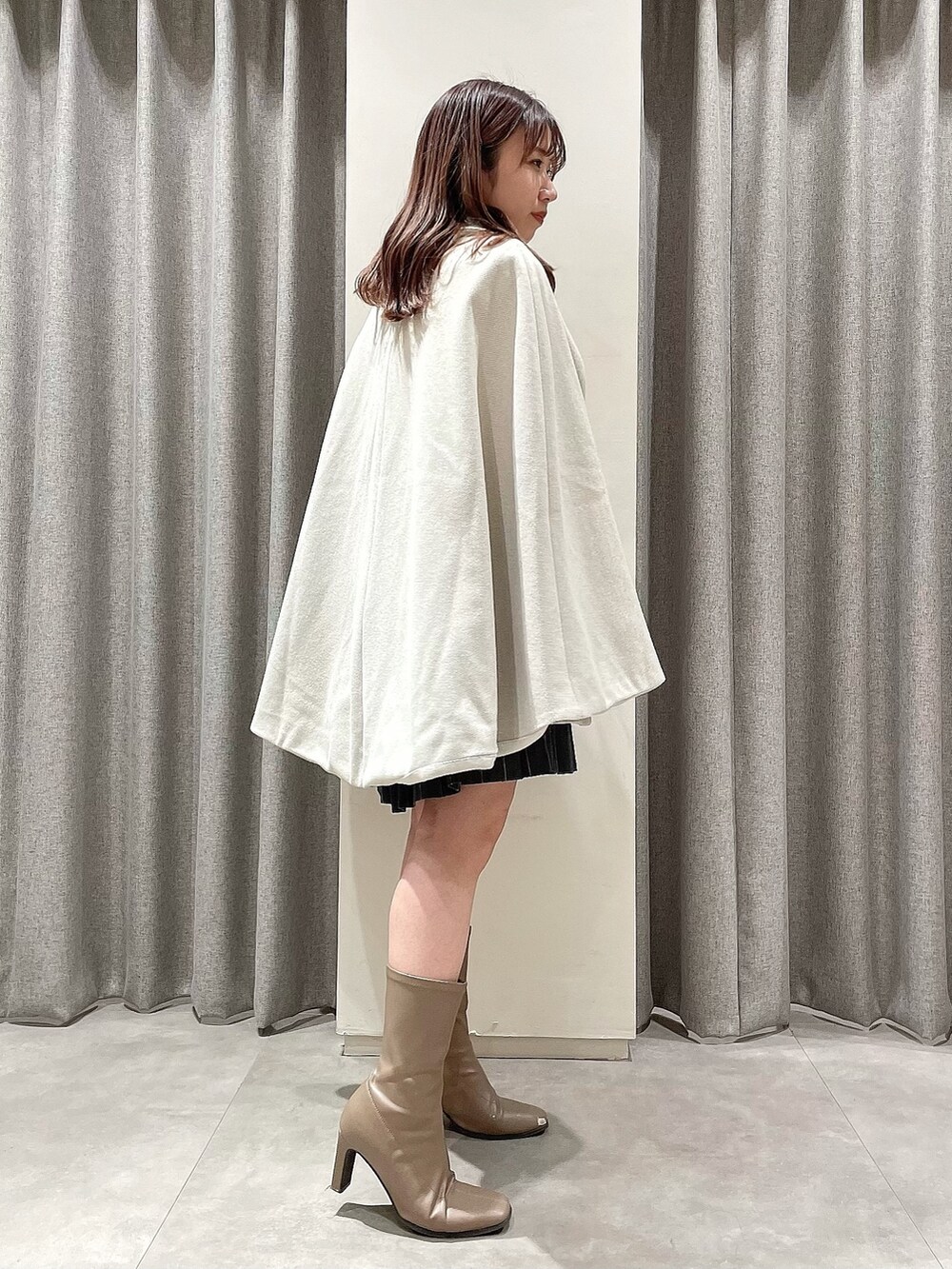 ホワイト系のポンチョ、ブラック系のニット/セーター、グレー系のスカートを着用したレディースの冬コーディネートの2枚目の写真