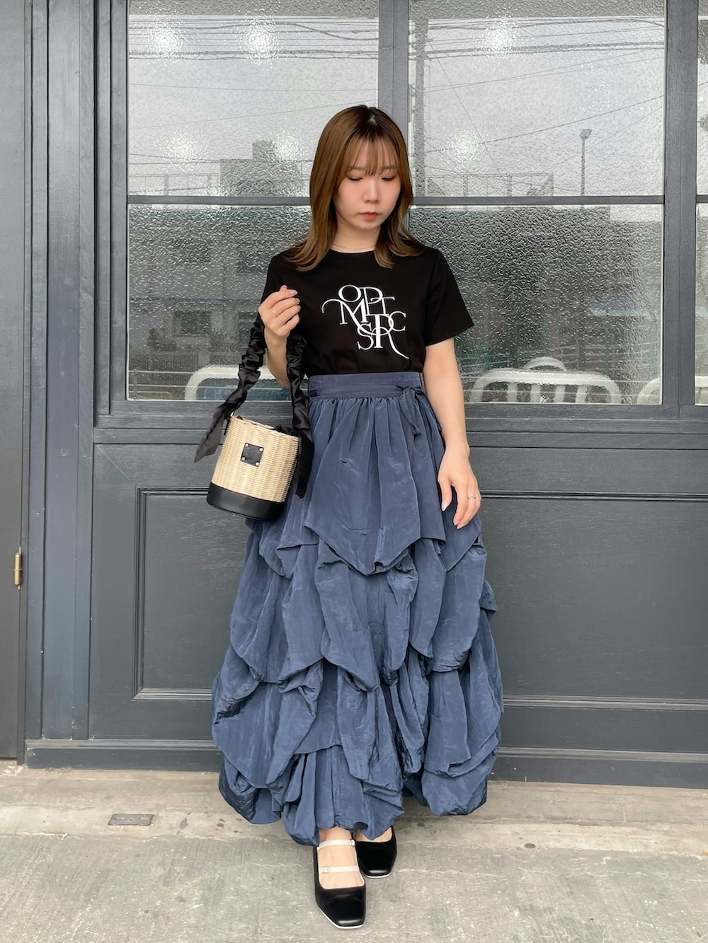 ブラック系のTシャツ/カットソー、ブラック系のかごバッグ、ブルー系のスカートを着用したレディースの夏コーディネートの3枚目の写真